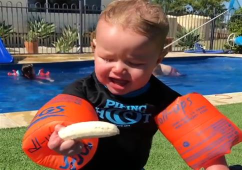 Kind versucht mit Schwimmflügeln eine Banane zu essen