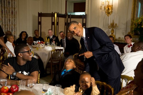 President Barack Obama jokes as a little boy sleeps in his chair during the Father's Day ice cream social in the State Dining Room of the White House, June 14, 2013. Students from the Becoming A Man (BAM) program in Chicago attend. (Official White House Photo by Pete Souza)